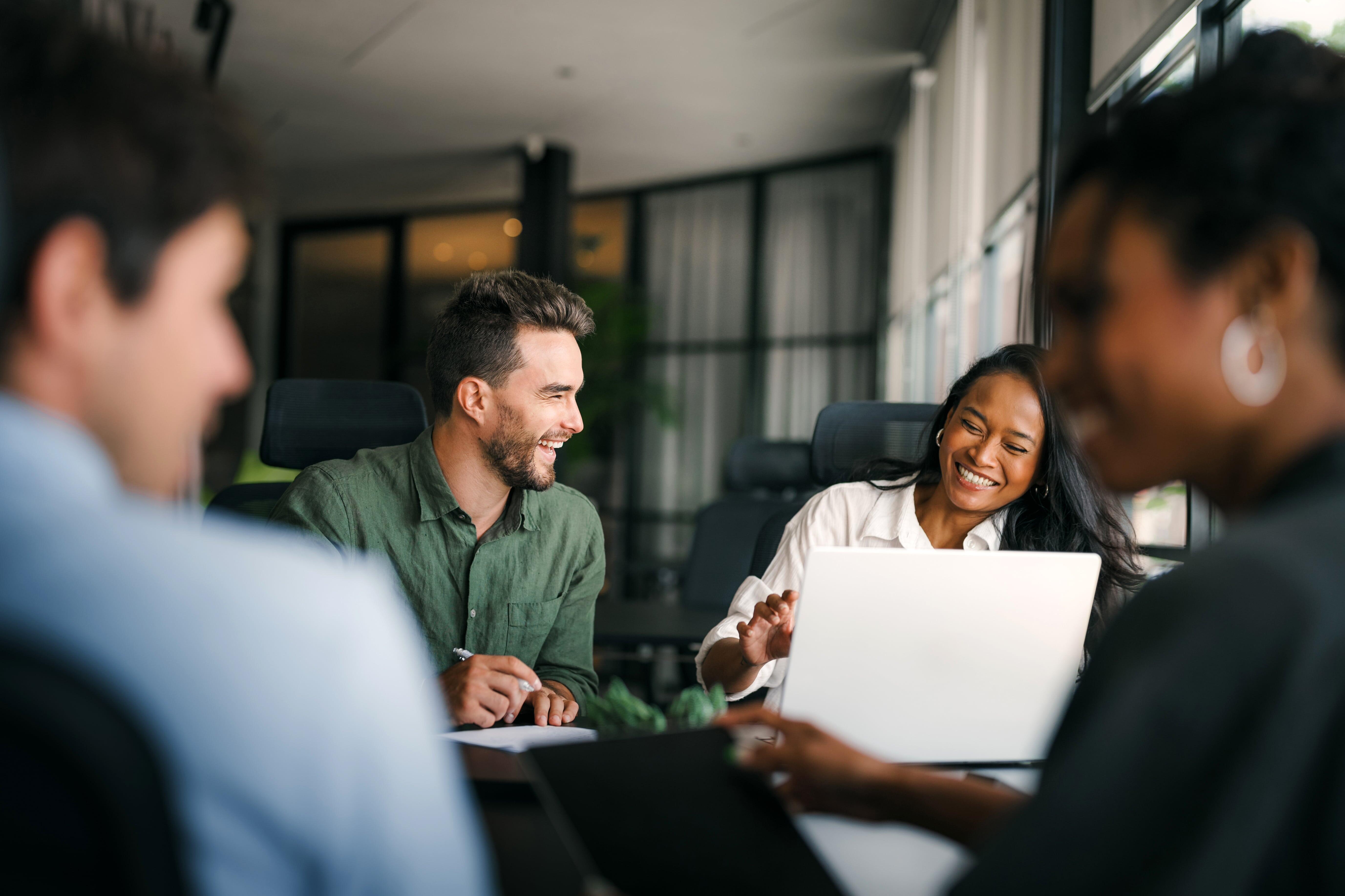 Profissionais sorrindo e conversando em equipe durante uma reunião de trabalho, representando o desenvolvimento de soft skills como comunicação e colaboração no ambiente corporativo.