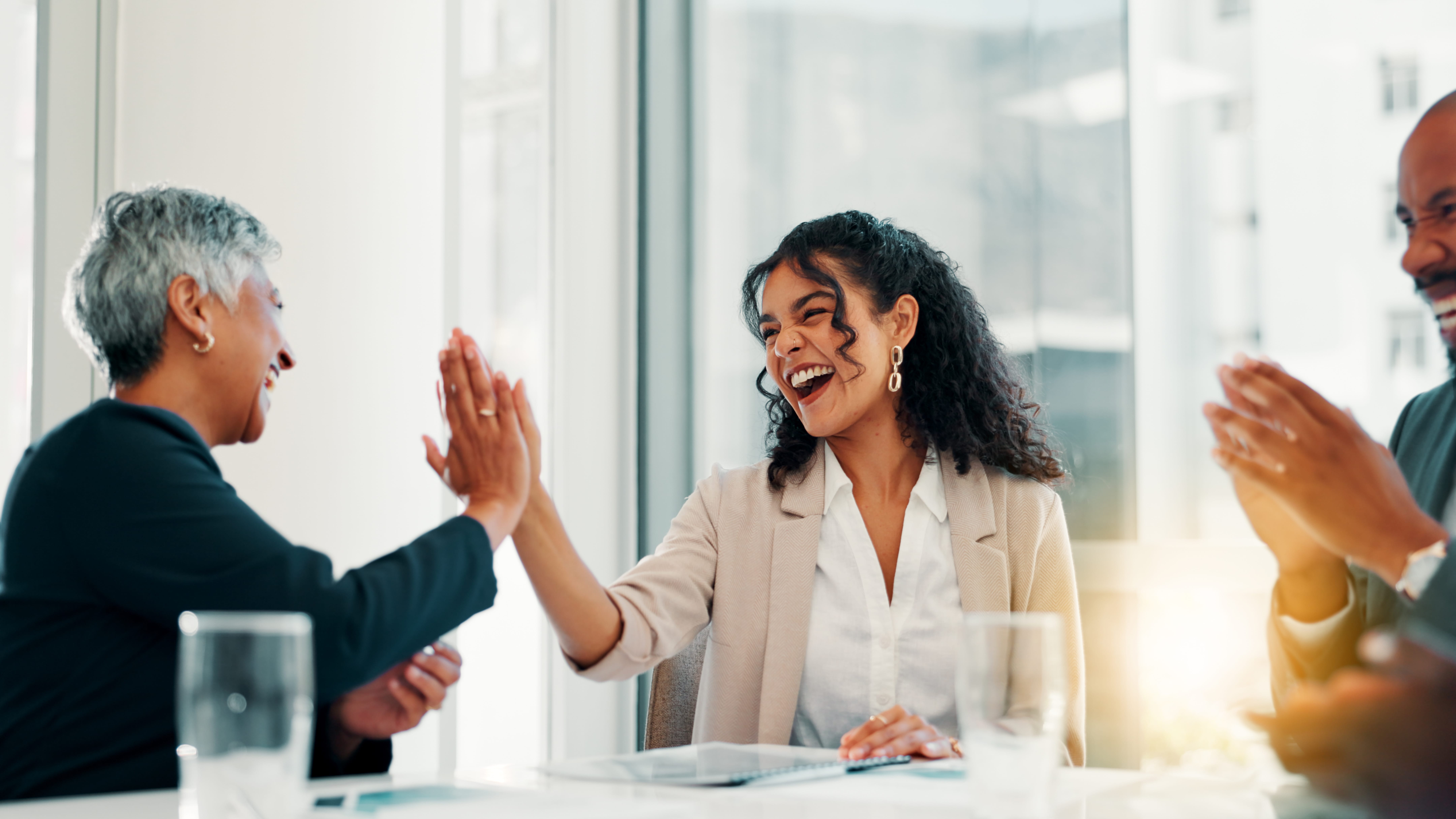 Mulher jovem sorridente recebe um high five de colega em ambiente corporativo, sendo reconhecida por seu desempenho. A imagem representa inteligência emocional no trabalho e o impacto positivo nas relações profissionais