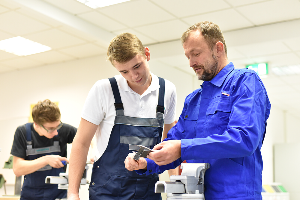 Um jovem observando atentamente uma outra pessoa demonstrar algo com um objeto na mão.