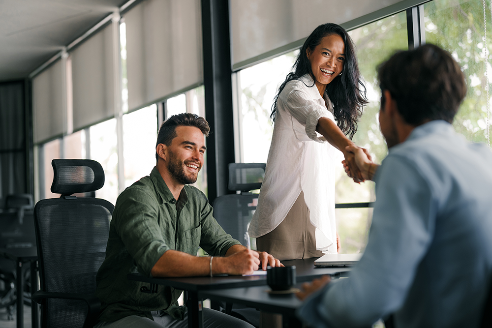 Mulher sorridente cumprimenta um recrutador em entrevista de emprego, após se preparar com um teste vocacional.