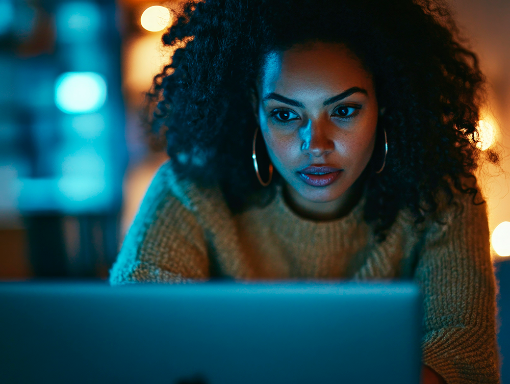 mulher olhando para a tela do computador, a luz da tela refletindo em seu rosto.